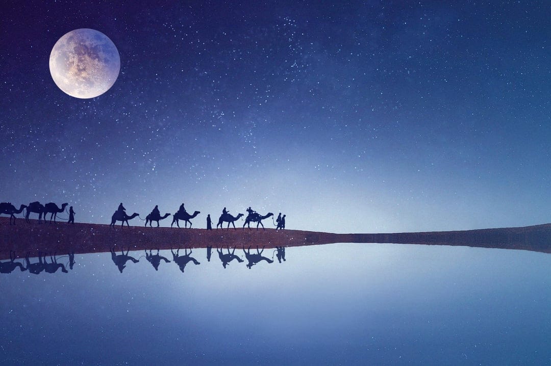 Camel caravan silhouettes walk past a massive full moon reflected in a calm desert oasis at night under stars.