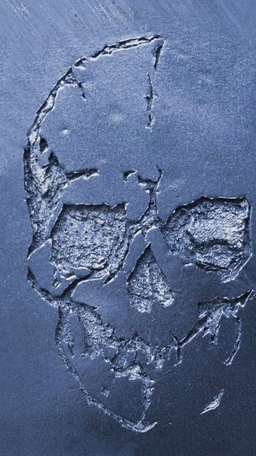 Weathered skull relief carved into a textured blue metallic surface with deep shadows in the eye sockets and jaw.