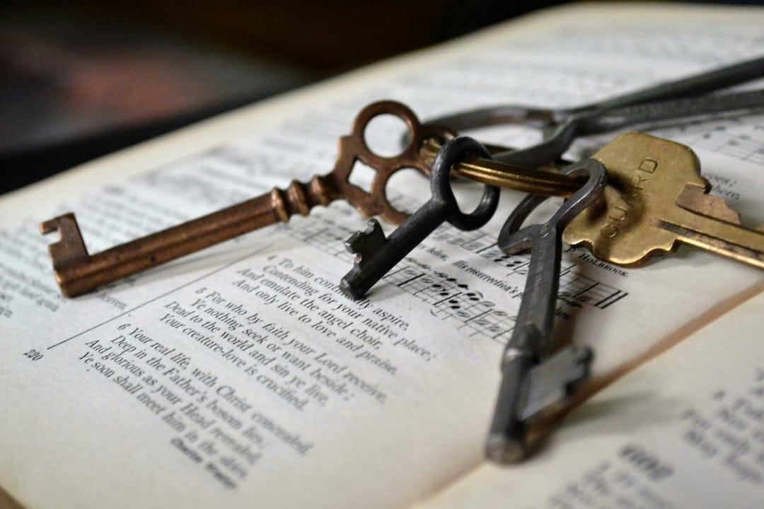 Vintage metal keys rest on the open pages of a hymnal book with musical notes under soft, warm lighting.