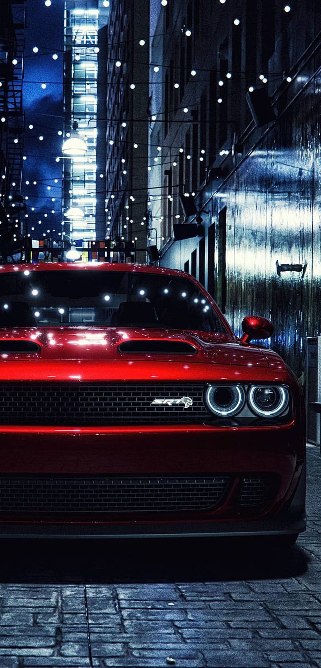 Red Dodge Challenger SRT Hellcat with glowing halo headlights parked in a dark city alley under string lights.