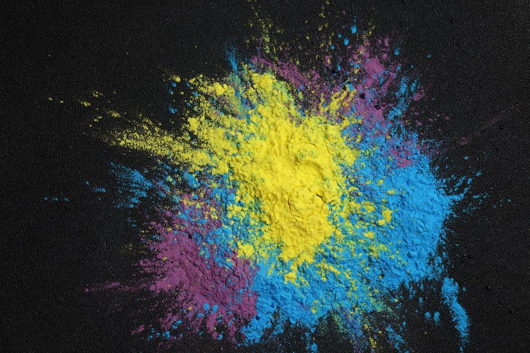 Cyan and magenta powder particles exploding outward against a solid black background with fine granular textures.