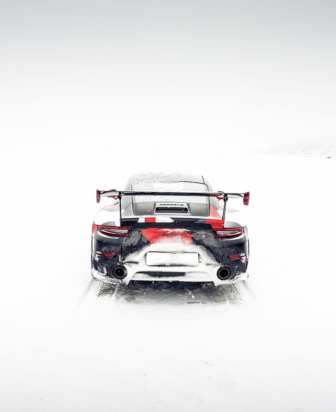 Porsche 911 GT2 RS with a black and red camo wrap driving on a snowy road with a large rear wing visible.
