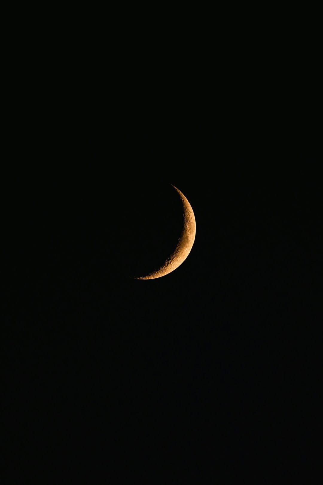 Golden crescent moon with visible crater textures suspended in a pitch black night sky, centered vertically.
