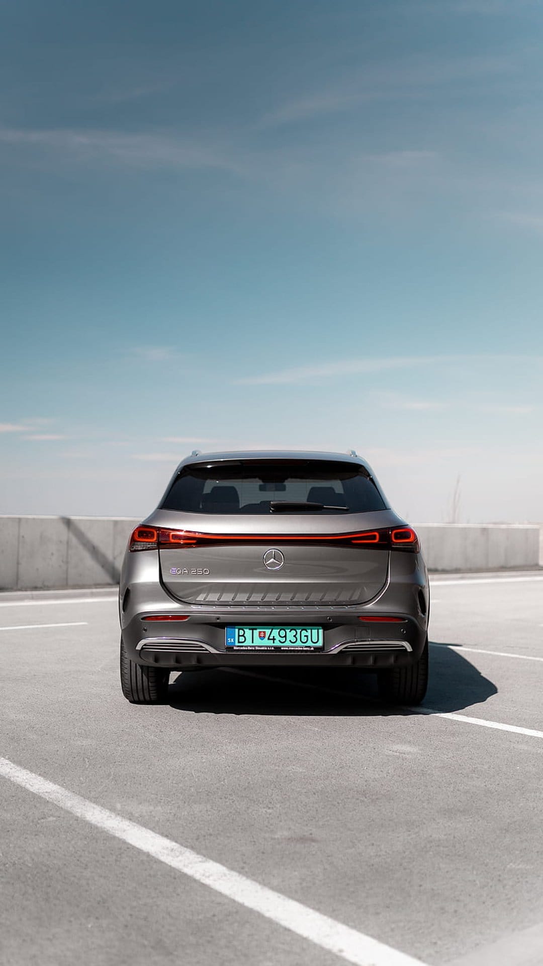 Mercedes-Benz EQA electric SUV with a glowing rear light bar parked on a rooftop under a clear blue sky.