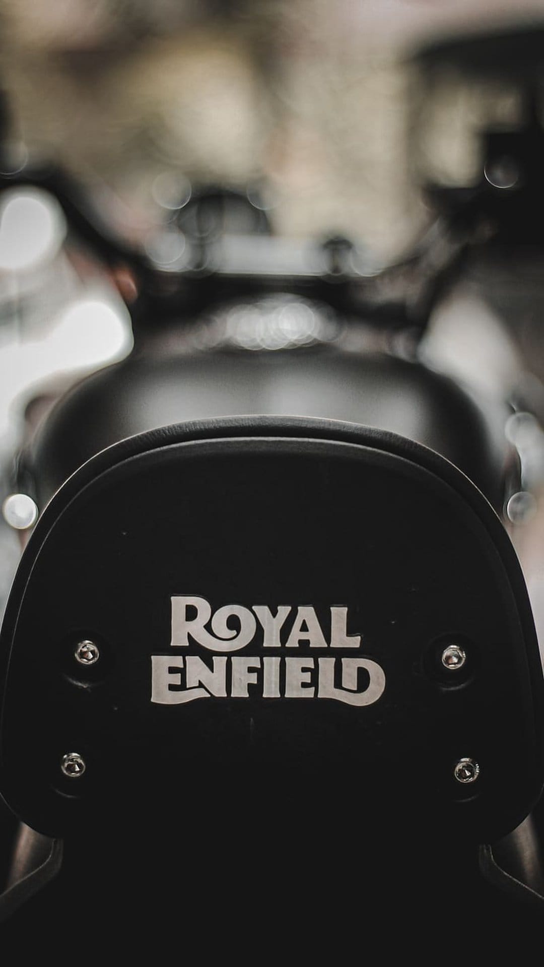 Royal Enfield silver metallic logo embossed on a black leather motorcycle seat backrest with blurred background.