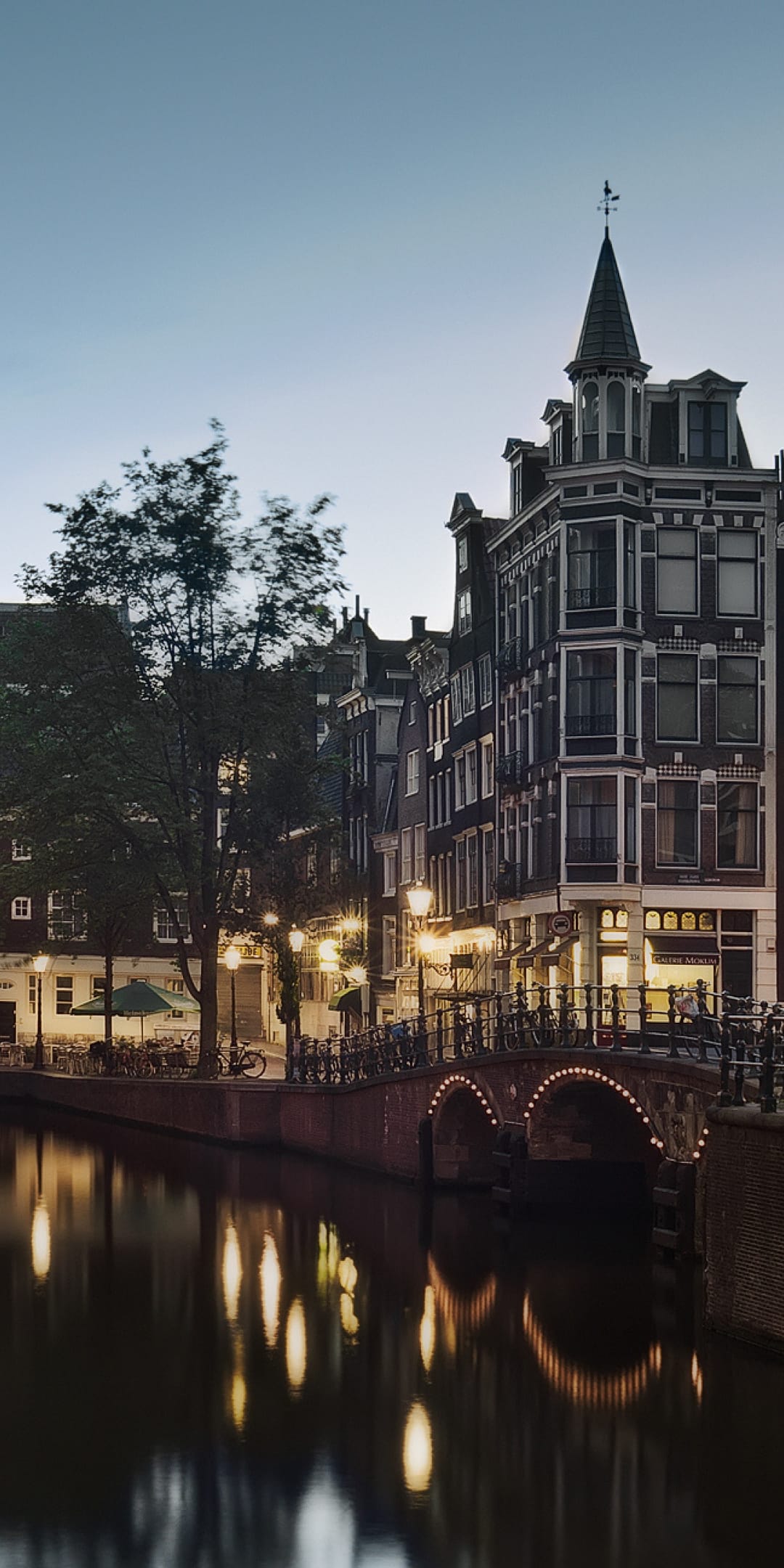 Traditional Dutch houses and an arched stone bridge reflecting in a dark canal under glowing streetlights.