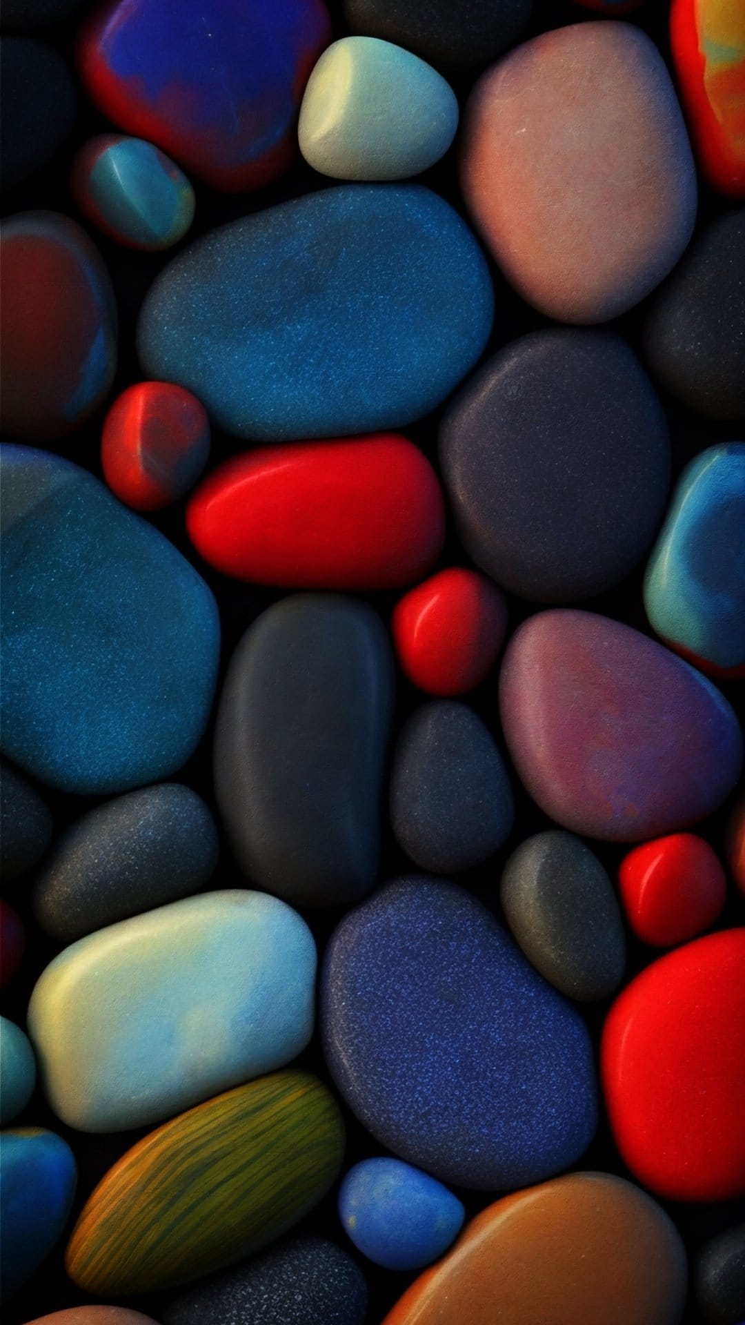 Smooth polished pebbles in blue, red, and pink hues overlap in a macro shot with glossy reflective surfaces.
