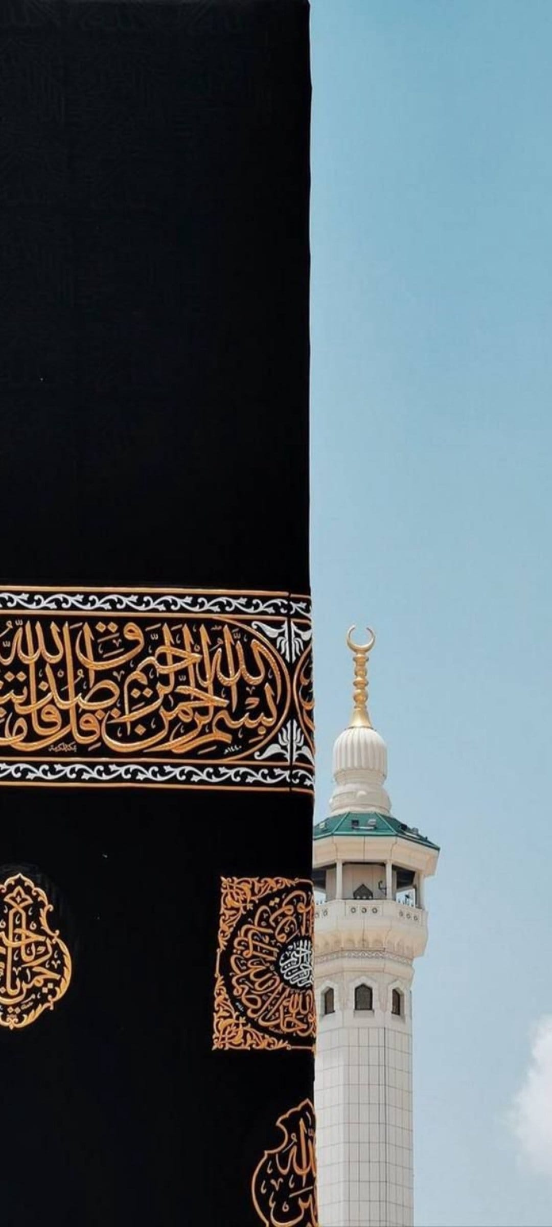 Black Kaaba Kiswah with gold calligraphy next to a white minaret and green roof under a clear blue sky.