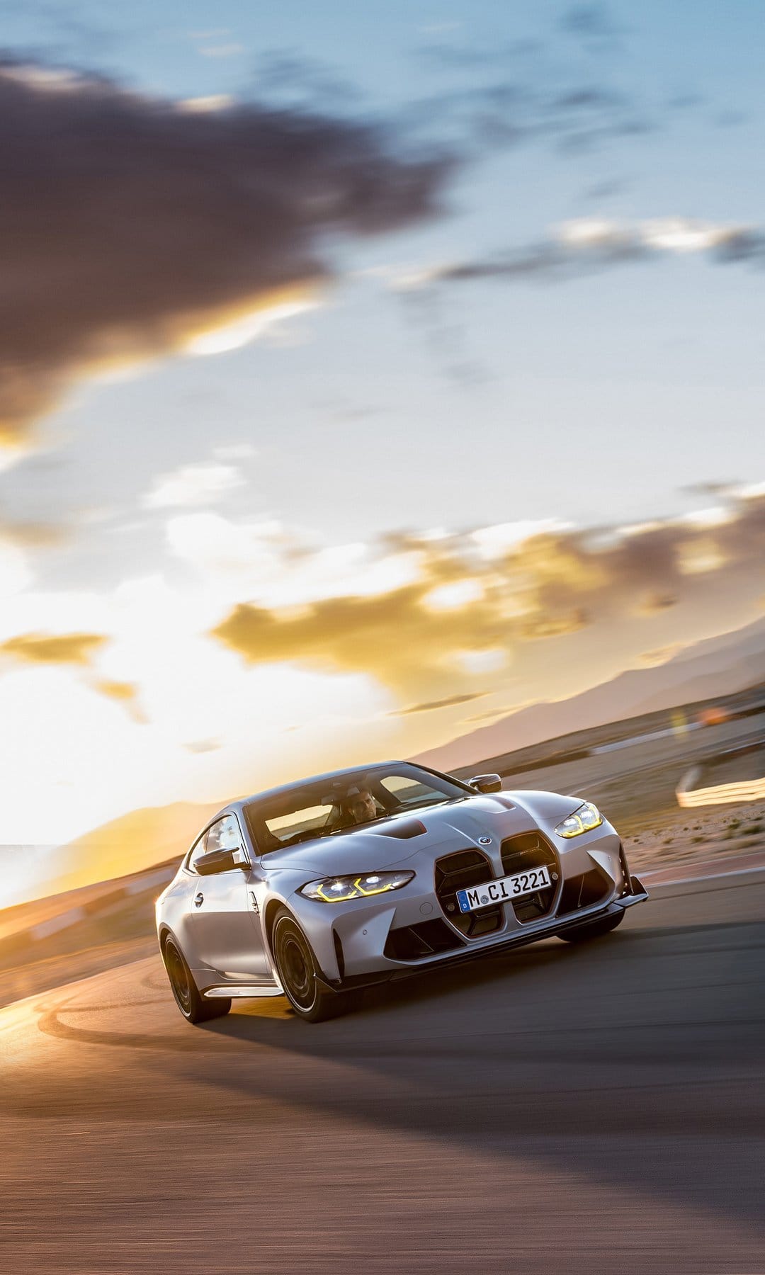Silver BMW M4 CSL drifting on a track at sunset with motion blur and warm golden lighting.