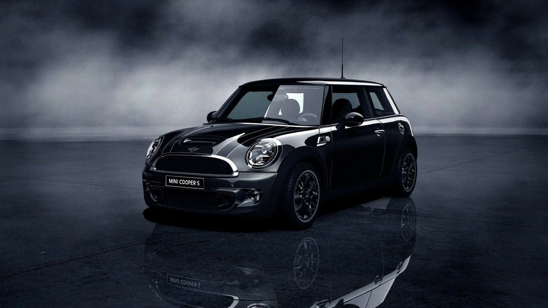 A black Mini Cooper S on a reflective floor against a dark foggy background with moody studio lighting.