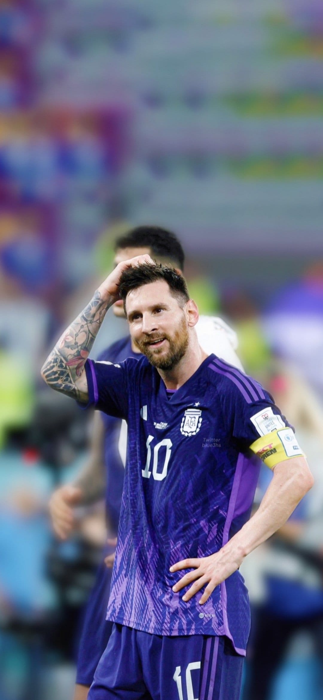 Lionel Messi wearing a purple Argentina jersey rests his hand on his head against a blurred stadium background.