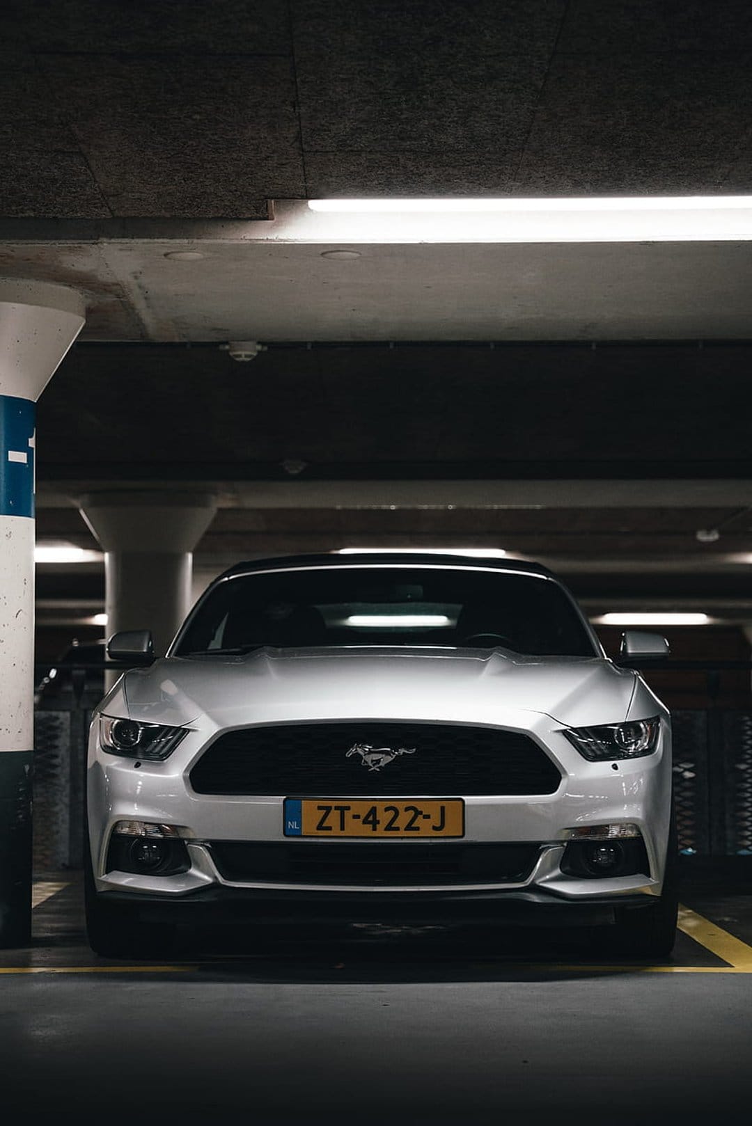 Silver Ford Mustang front grille and headlights in a dimly lit underground garage with cool fluorescent lighting.