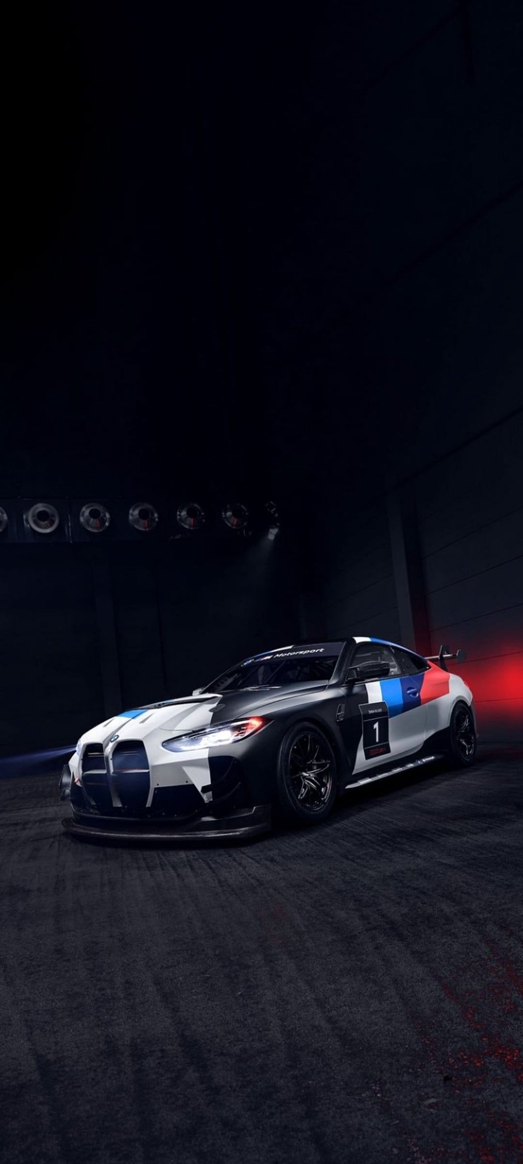 BMW M4 GT3 race car with black and white camouflage livery and number one decal in a dimly lit studio.
