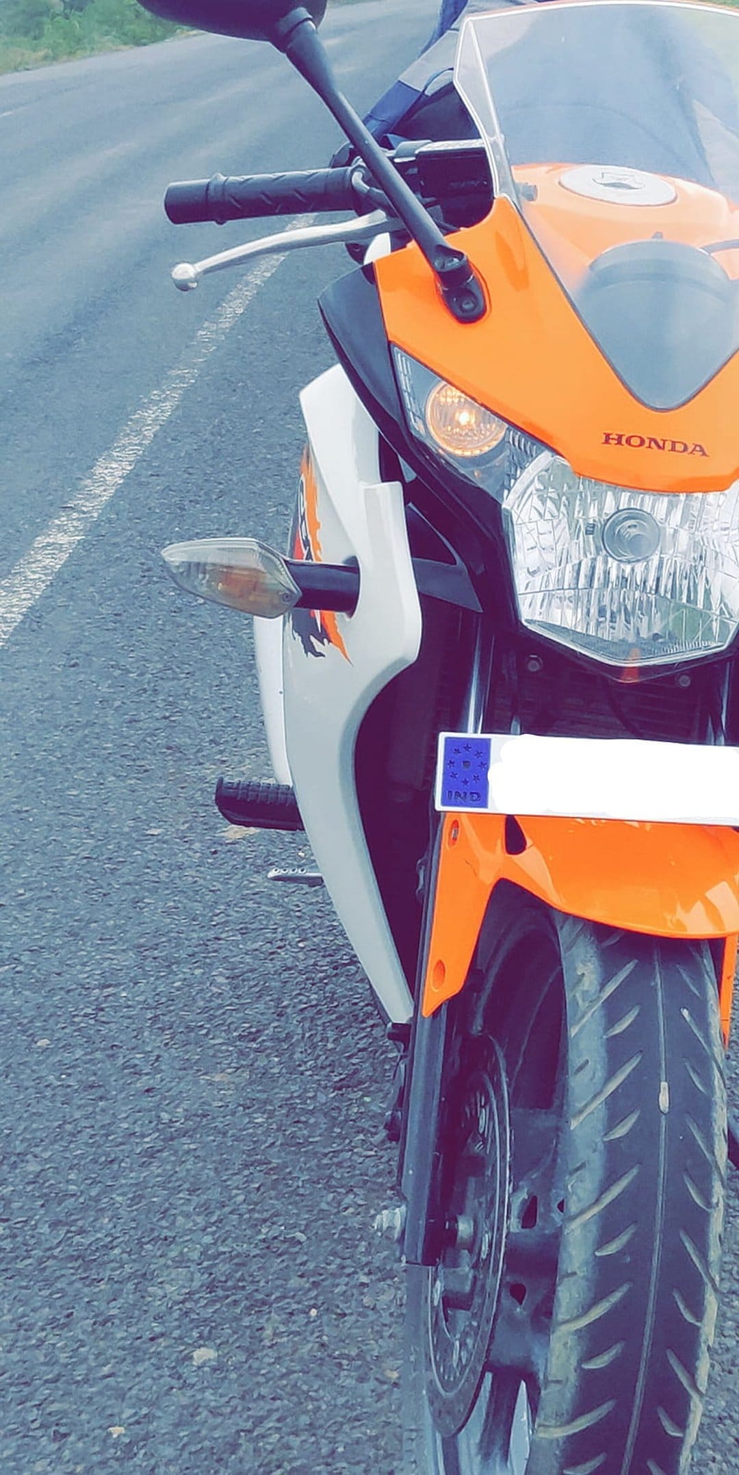 Honda CBR motorcycle front view features a bright orange fairing, LED headlight, and handlebars on an asphalt road.