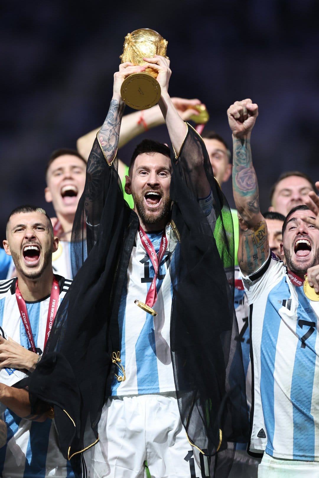 Lionel Messi wears a black Bisht while lifting the gold FIFA World Cup trophy amidst falling golden confetti.