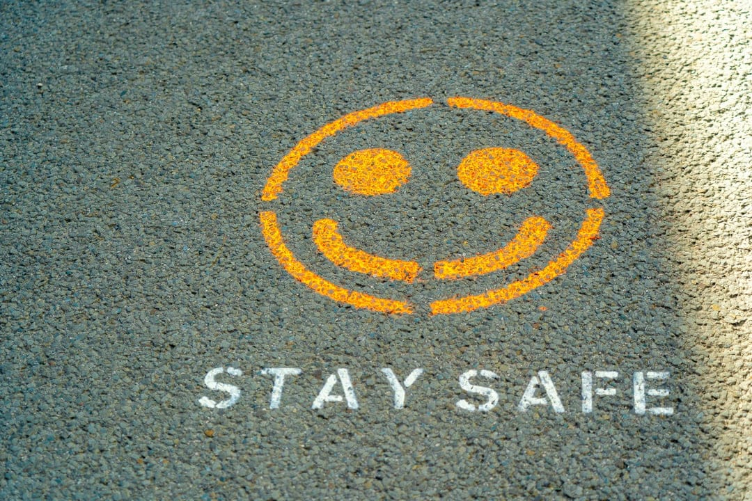 Vibrant orange smiley face stencil with white Stay Safe text on dark asphalt pavement with soft shadows.