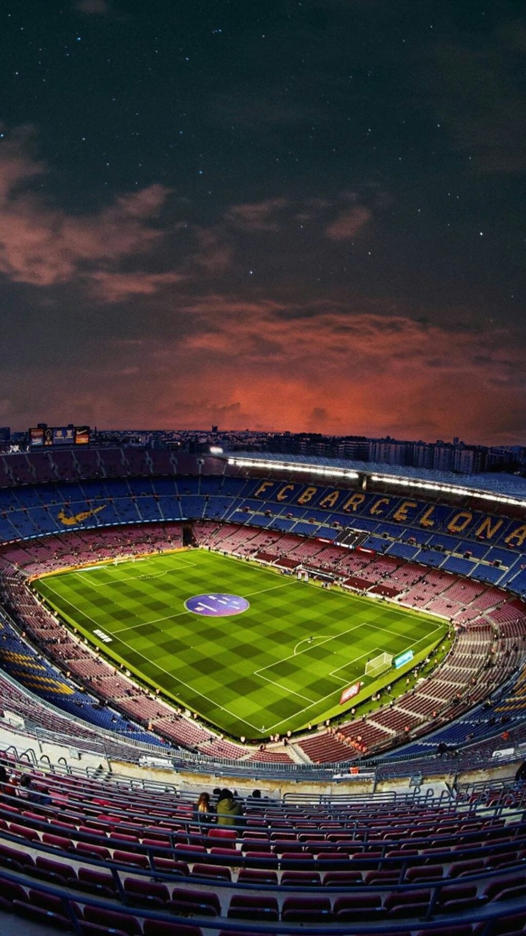 Camp Nou stadium seats in red and blue surround a green pitch under a starry dusk sky with glowing stadium lights.