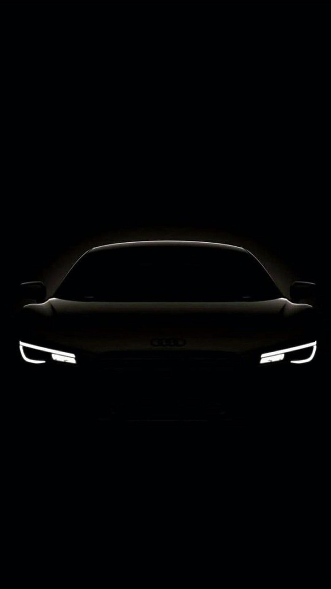 Audi R8 sports car silhouette with glowing LED headlights visible against a dark black night background.