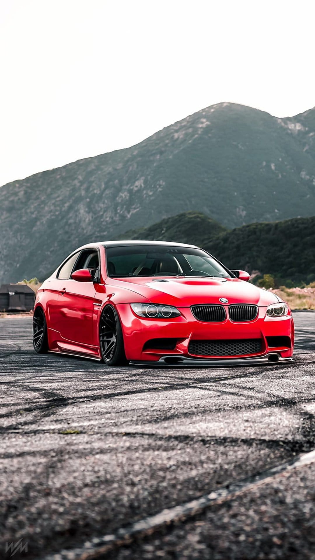 Red BMW M3 drifting on a rough asphalt road against a backdrop of hazy, jagged mountains under a clear sky.