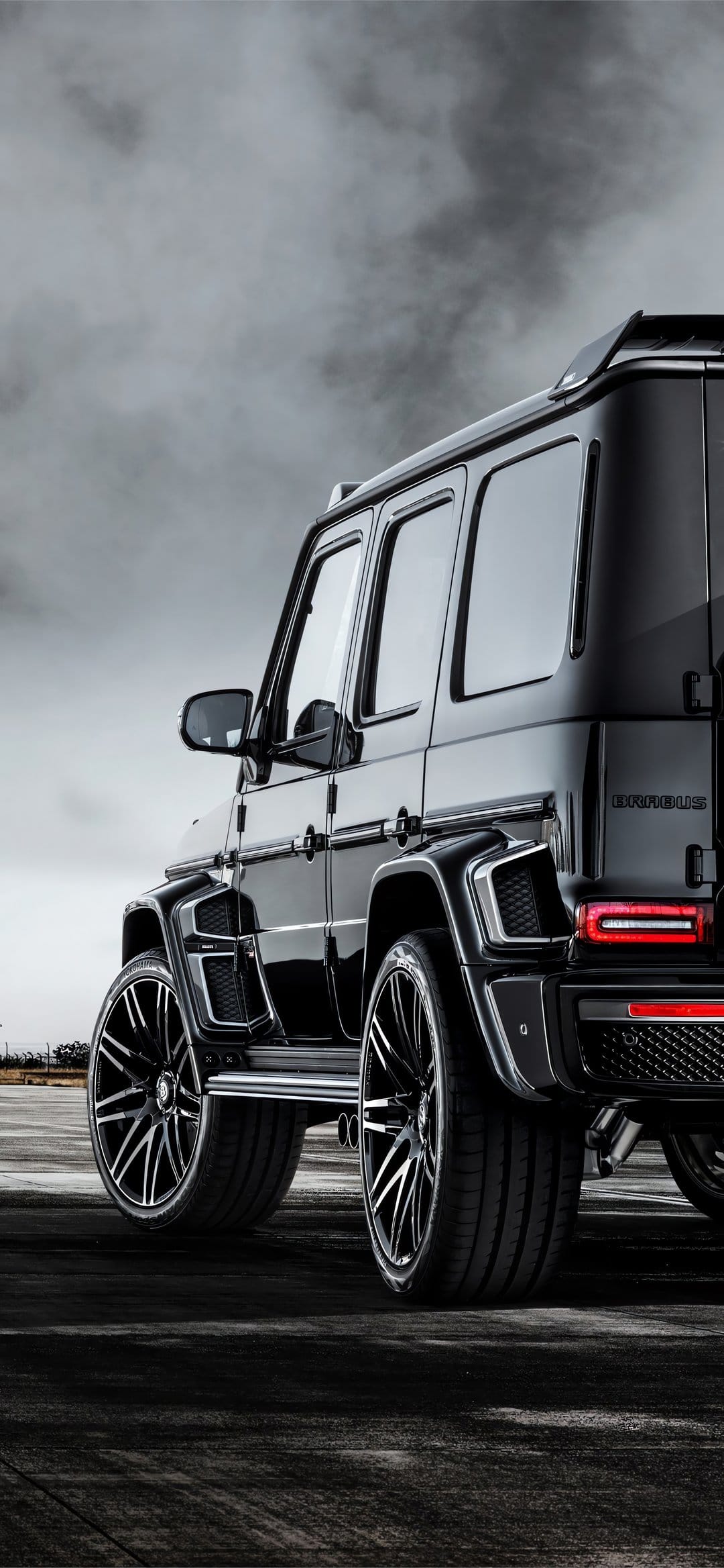 Black Brabus Mercedes G-Class SUV with large black wheels and a wide body kit against a cloudy grey sky.