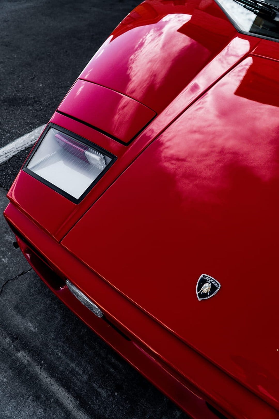 Red Lamborghini Countach hood featuring the gold raging bull shield with sky reflections on polished paint.