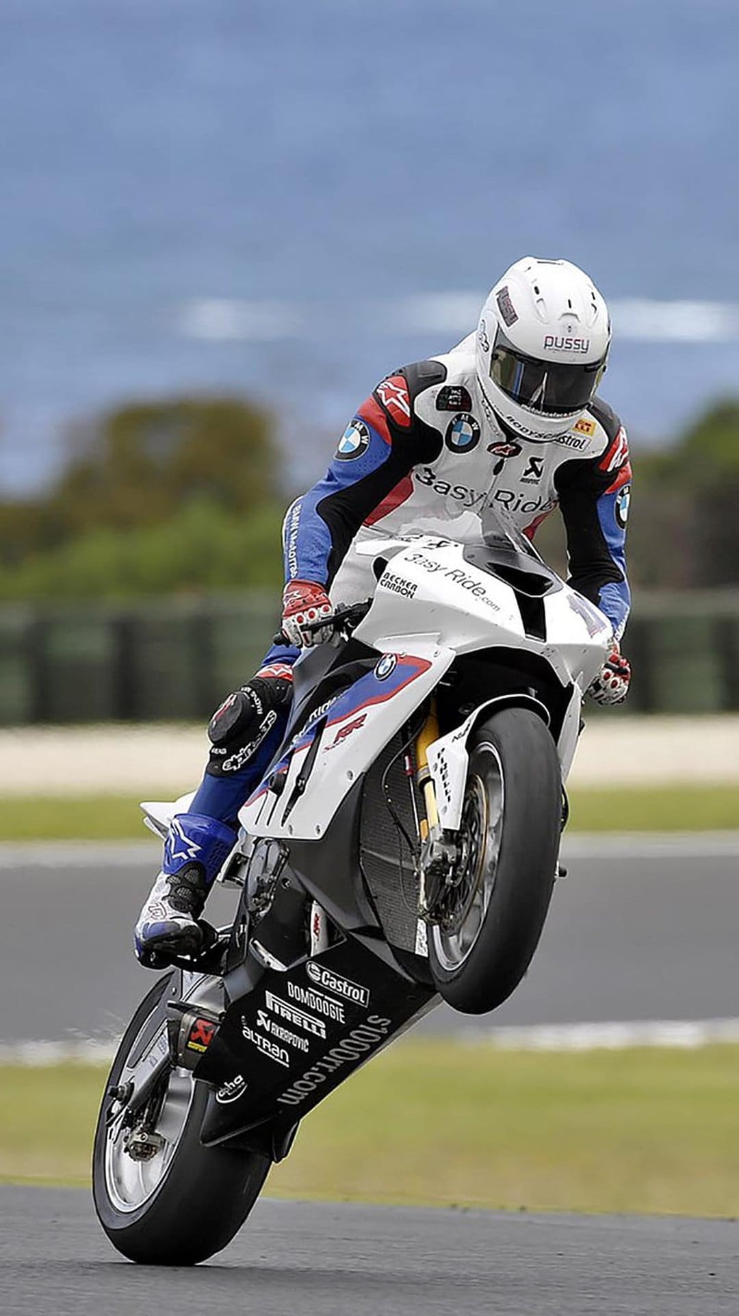 Motorcycle racer performing a wheelie on a white BMW S1000RR superbike during a high-speed track race event.