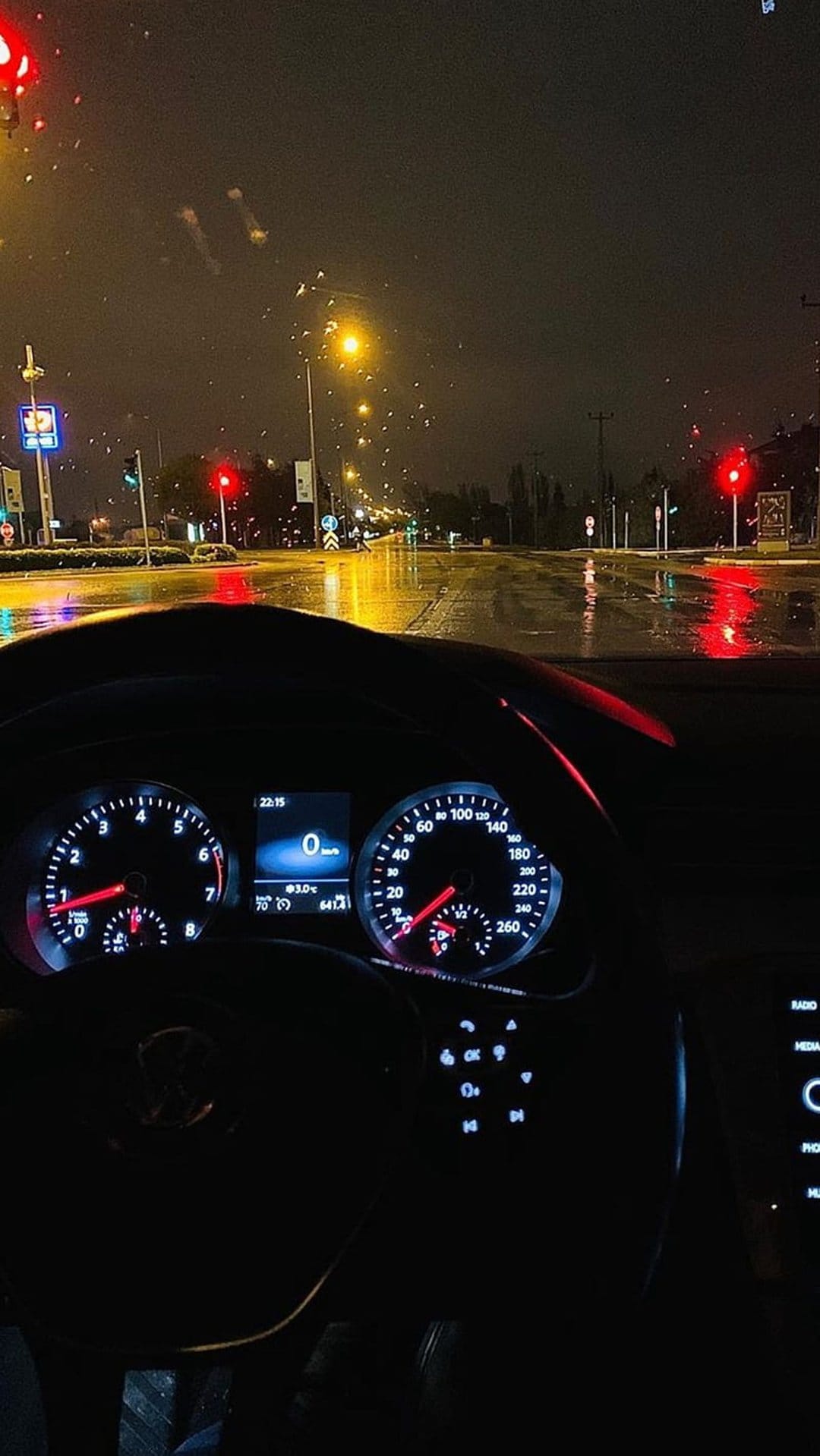 Raindrops on a car windshield overlook wet city streets with glowing dashboard lights and traffic reflections.