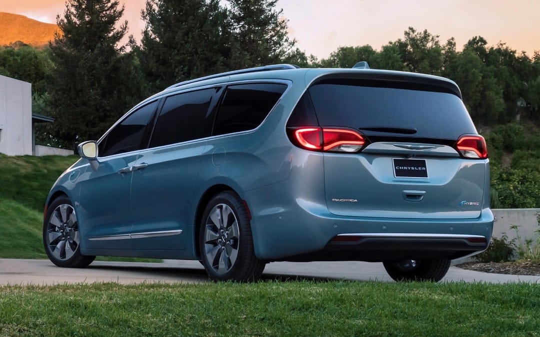 Light blue Chrysler Pacifica Hybrid minivan parked on a driveway at sunset with glowing red taillights.