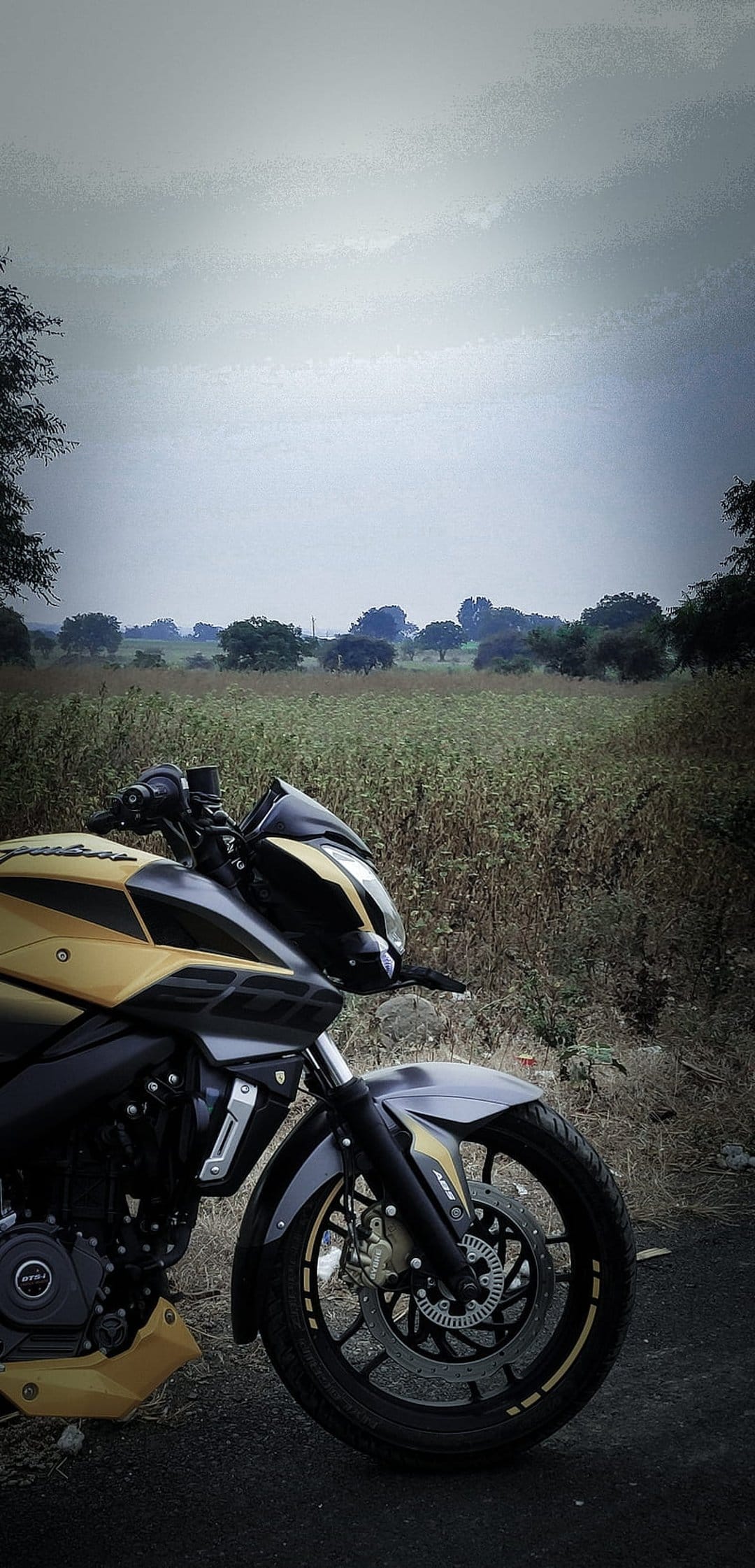 Black and gold sports motorcycle parked on a paved road beside a dry grassy field under a dark overcast sky.