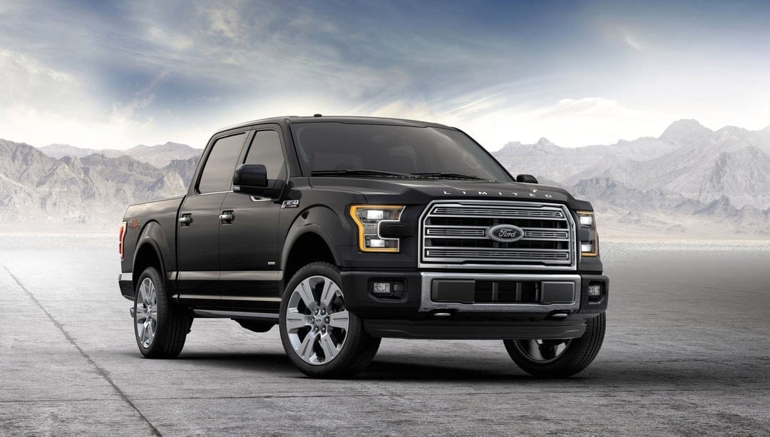 Black Ford F-150 Limited truck parked on a desert flat with mountains under a soft blue sky.