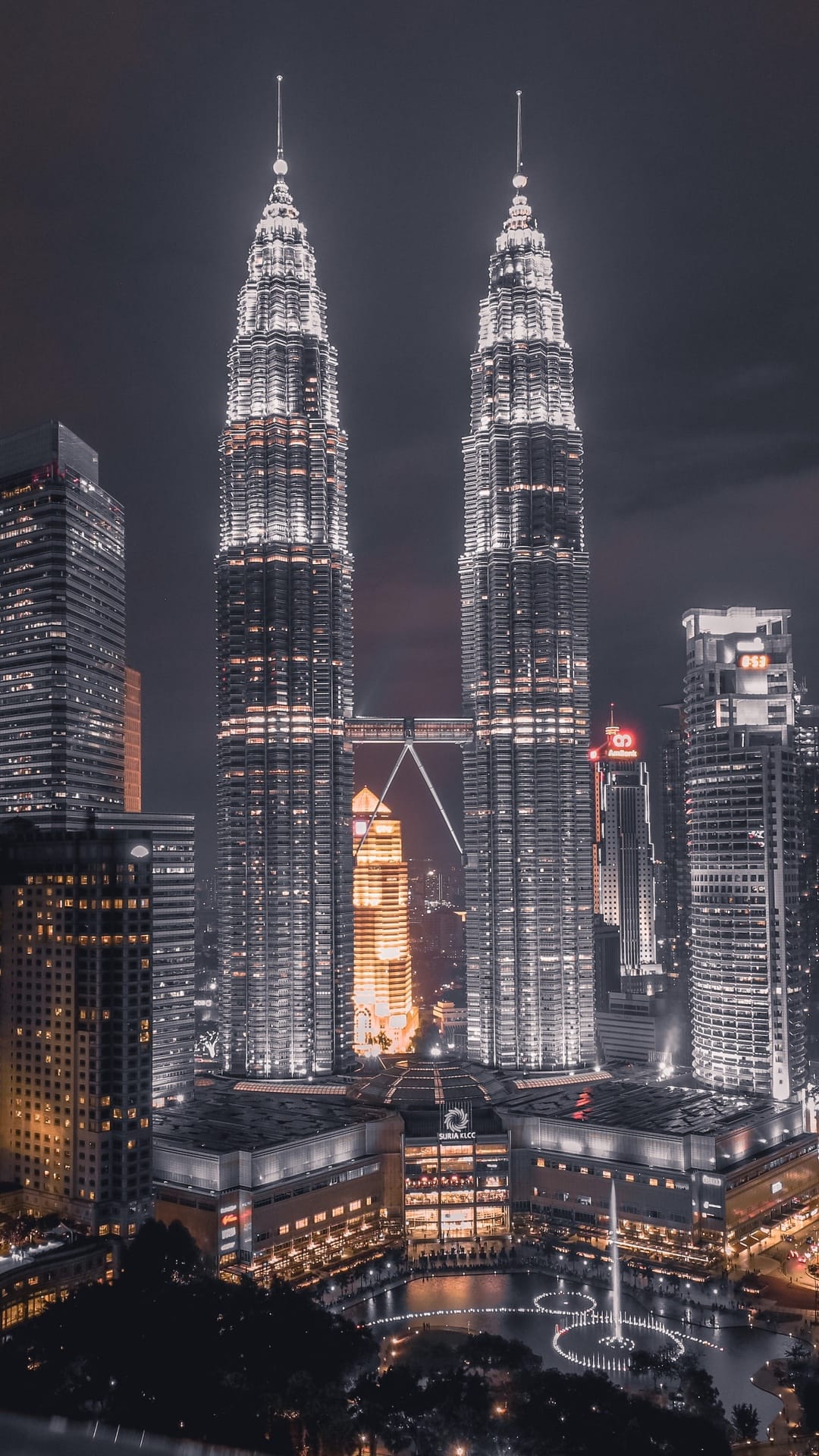 Petronas Twin Towers shine with bright white lights above a dark city skyline at night with a glowing skybridge.