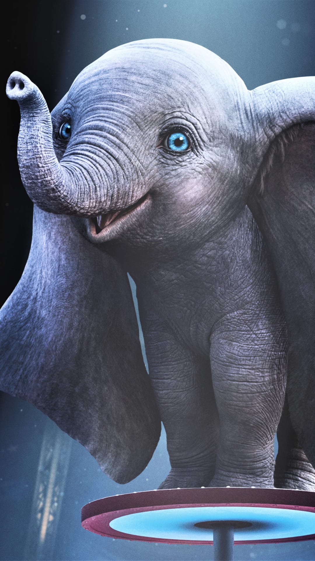 Baby elephant with large blue eyes and floppy ears stands on a circus platform with a curved trunk and soft lighting.