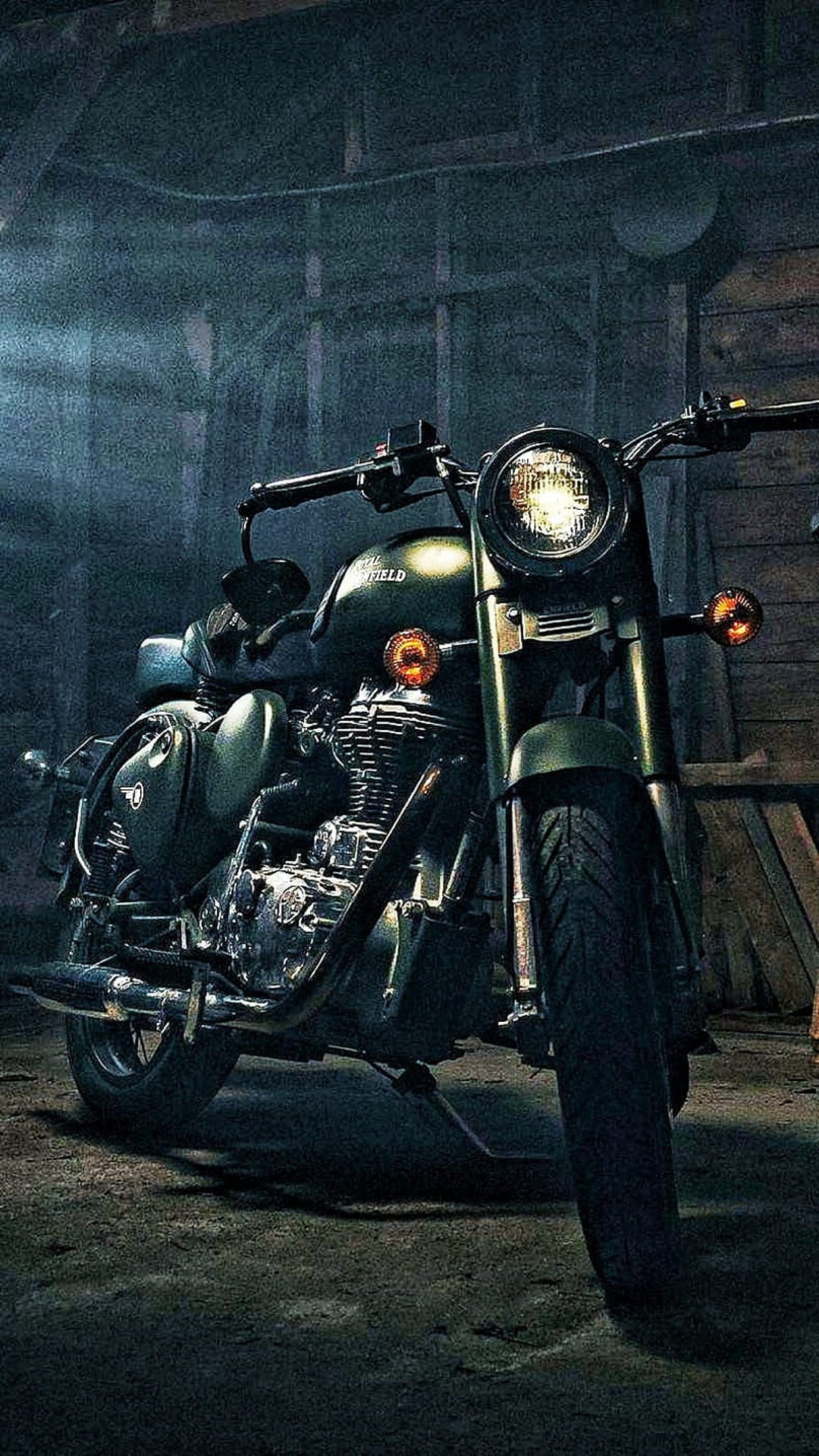 Olive green Royal Enfield motorcycle with chrome details parked in a dimly lit, rustic workshop garage.