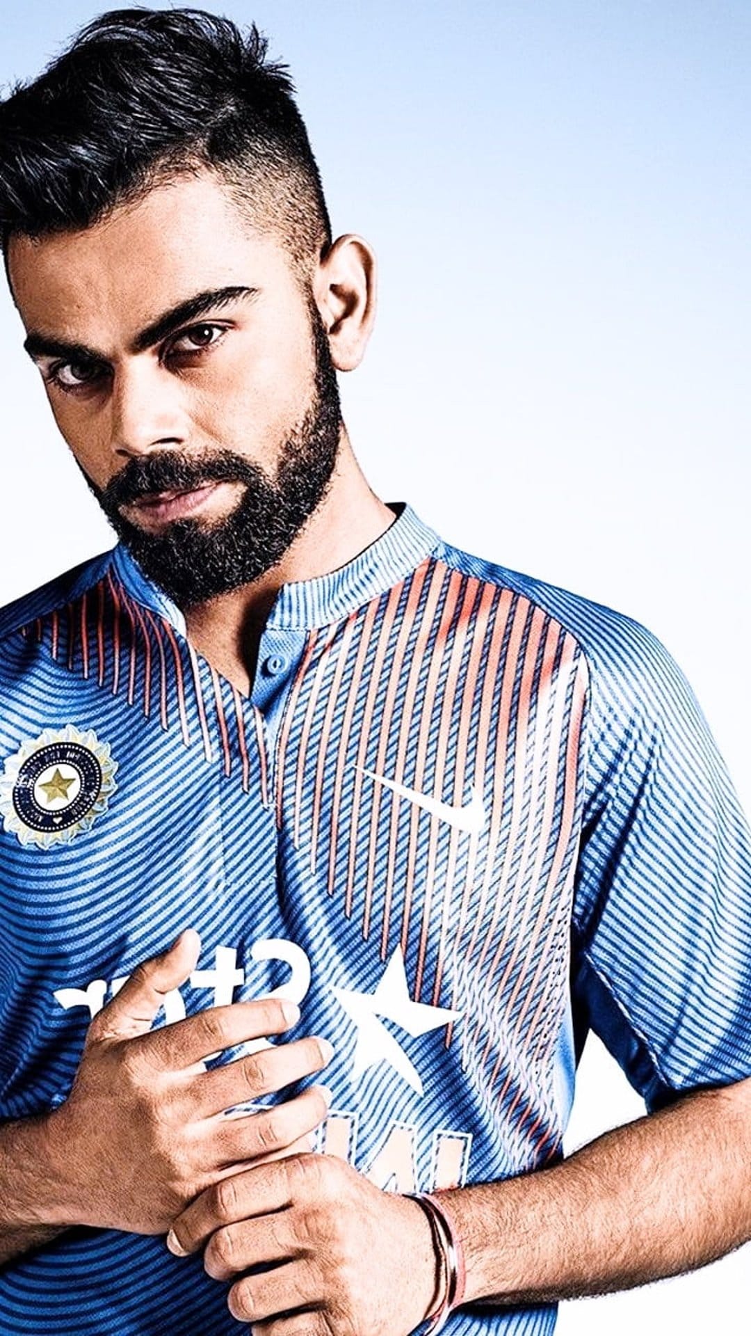 Virat Kohli wearing a blue Indian cricket jersey with a focused expression and groomed beard in a close-up portrait.