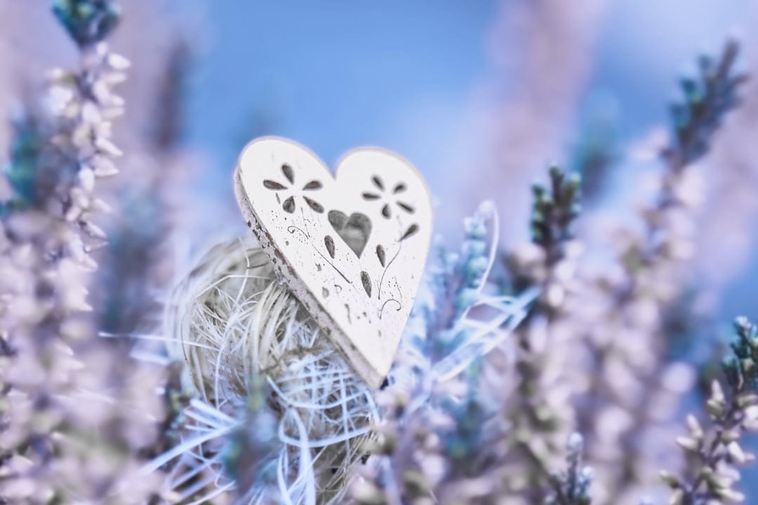 Intricately carved white floral heart resting on a twine ball within a soft-focus purple lavender field.