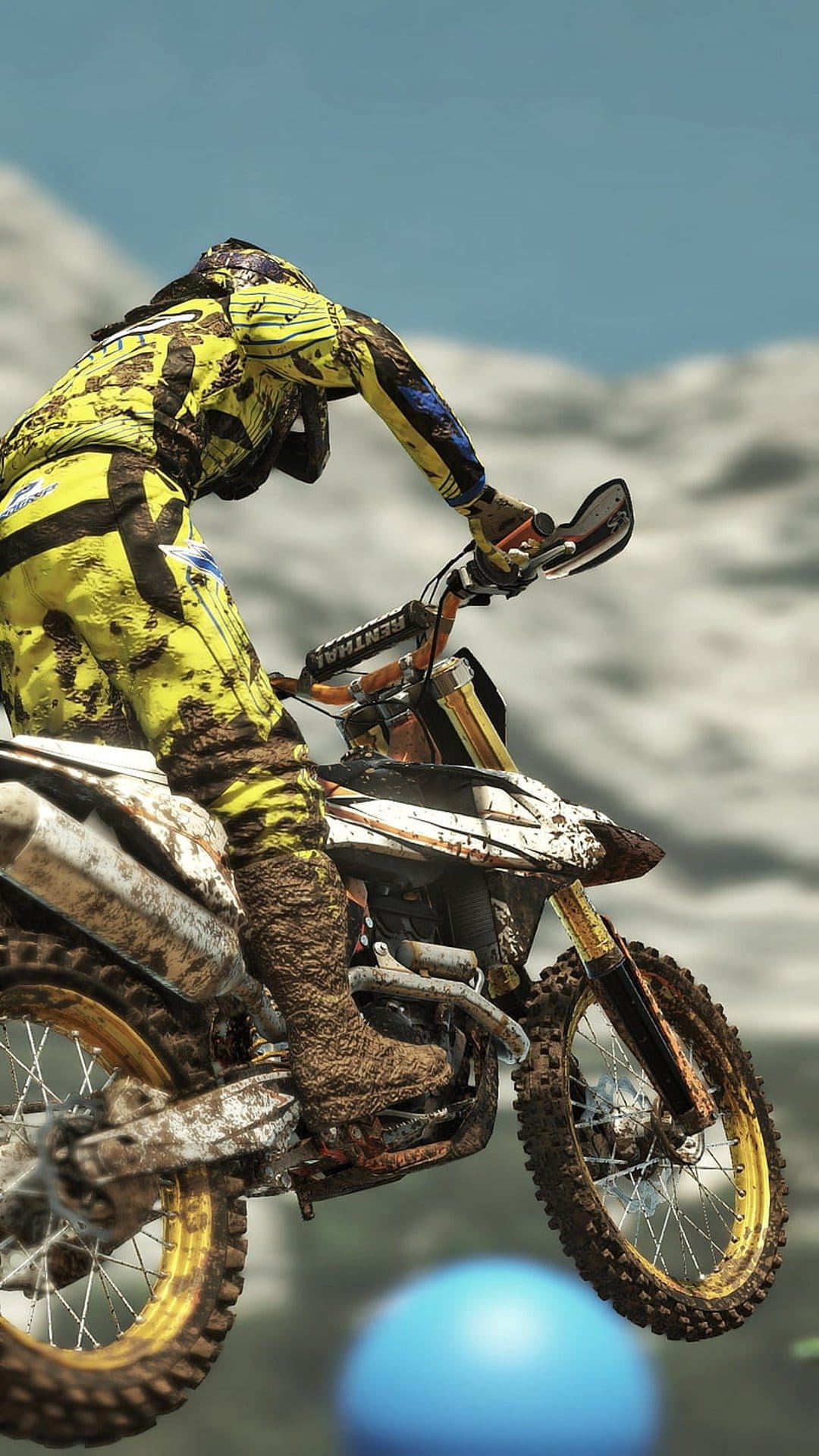 Motocross rider in mud-splattered yellow gear jumps a dirt bike with gold spokes against a clear sky.
