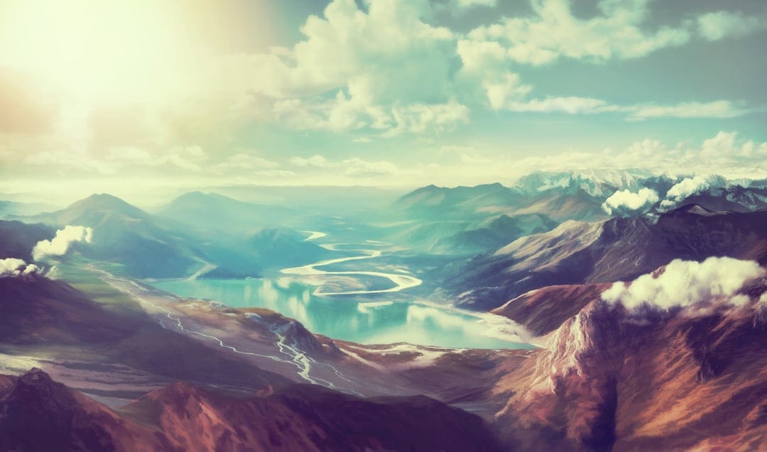 Winding blue river flows through a sun-drenched mountain valley under a soft cloudy sky at golden hour.