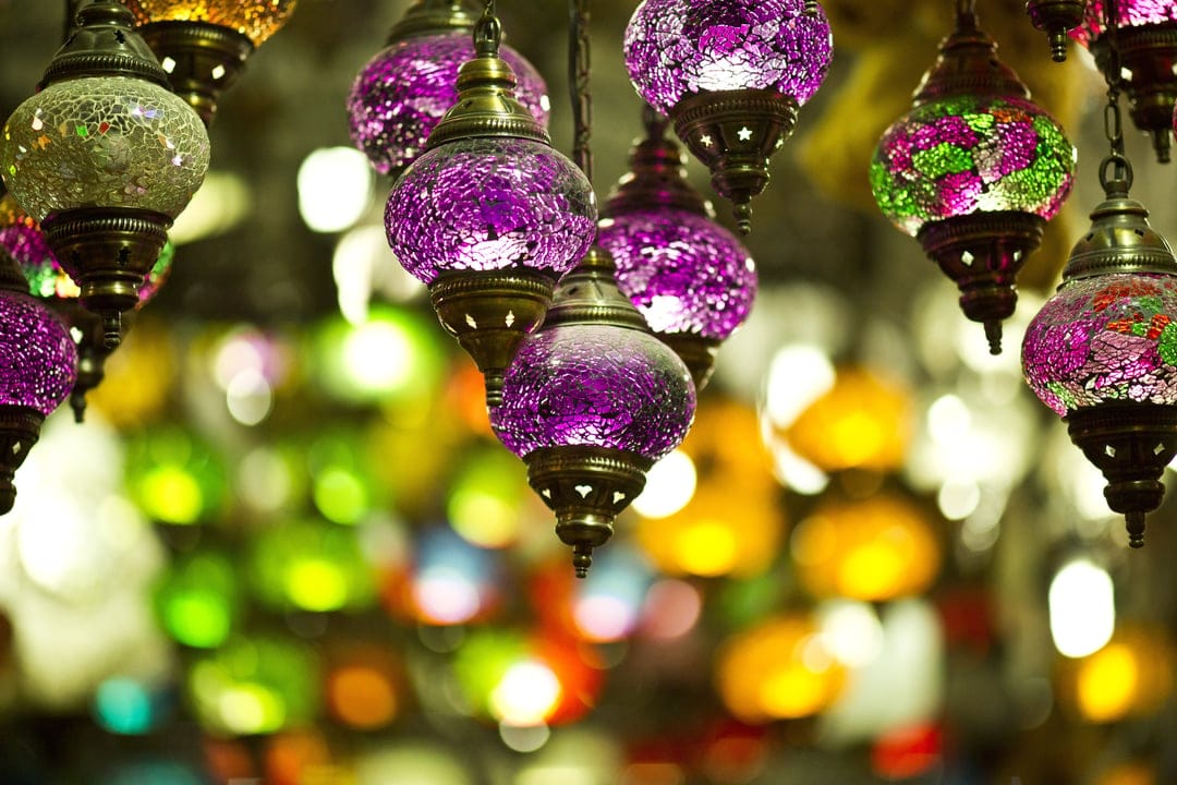 Turkish mosaic lamps with purple and green glass patterns glow brightly against a blurred market background.