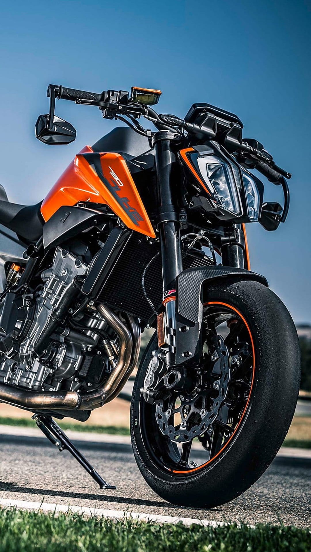 KTM 790 Duke motorcycle shows orange fairings and an exposed engine block under a clear blue sky atmosphere.