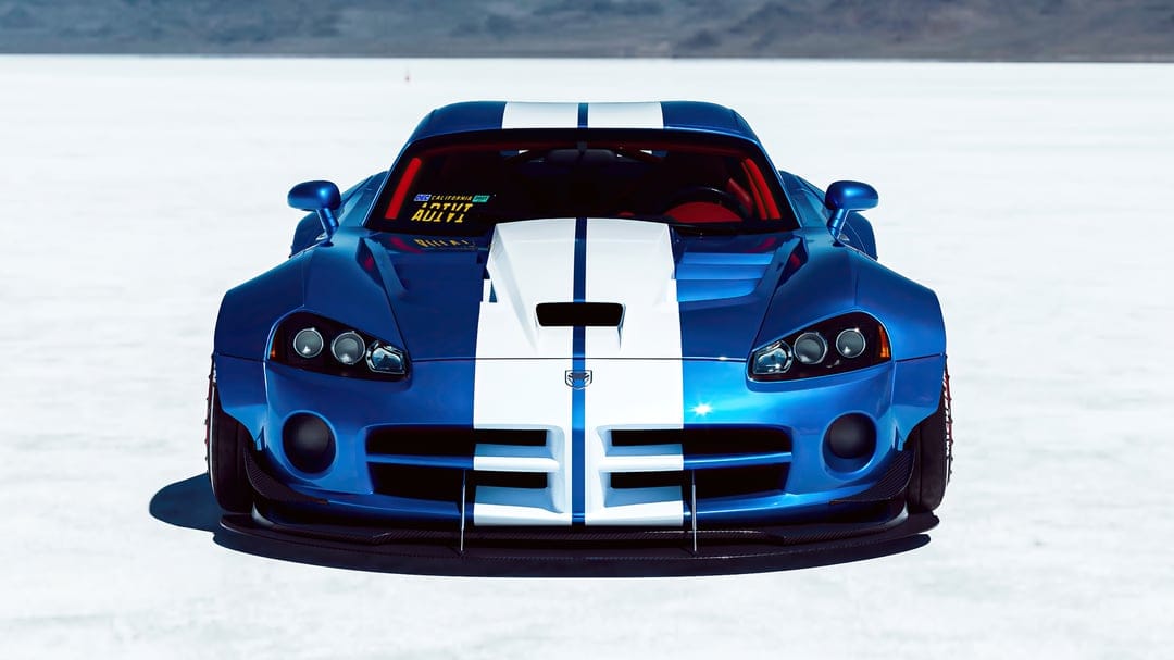 Front view of a blue widebody Dodge Viper with white racing stripes on flat white salt plains under bright sun.
