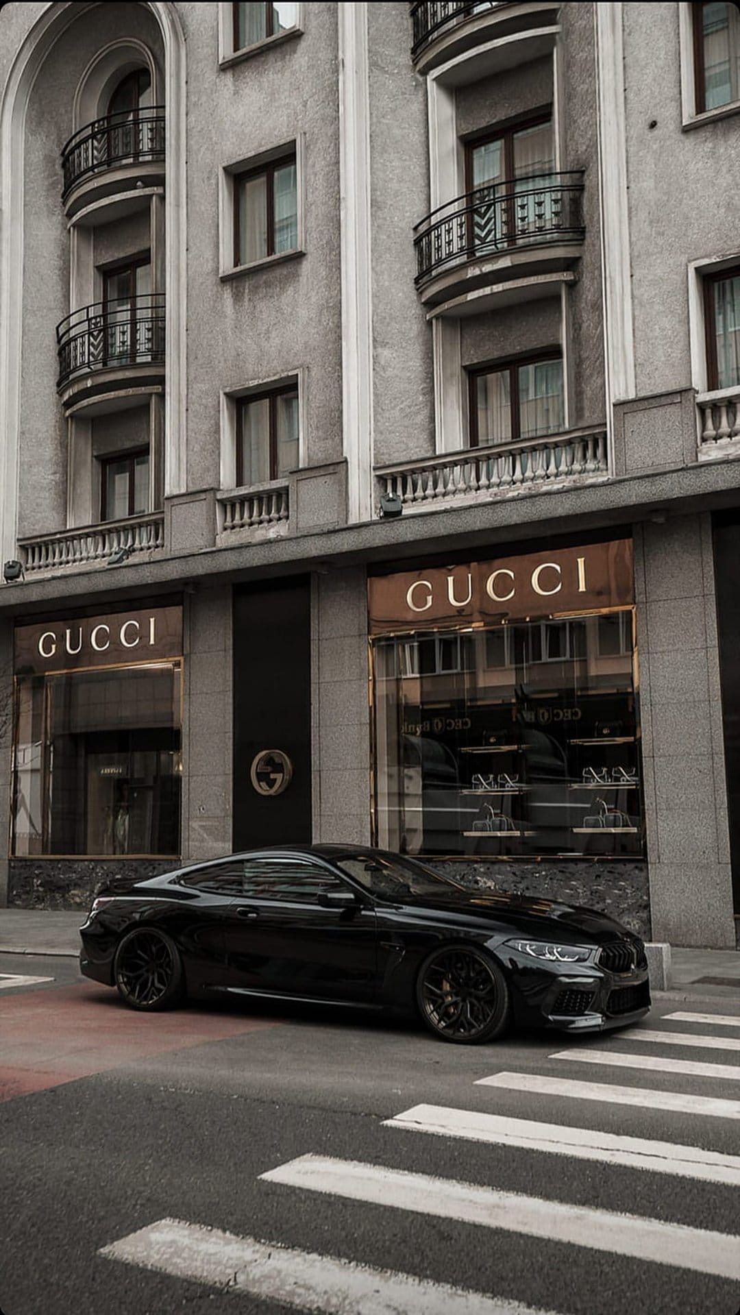Black luxury sports car parked outside a Gucci boutique with classical architecture and gold shop lighting.
