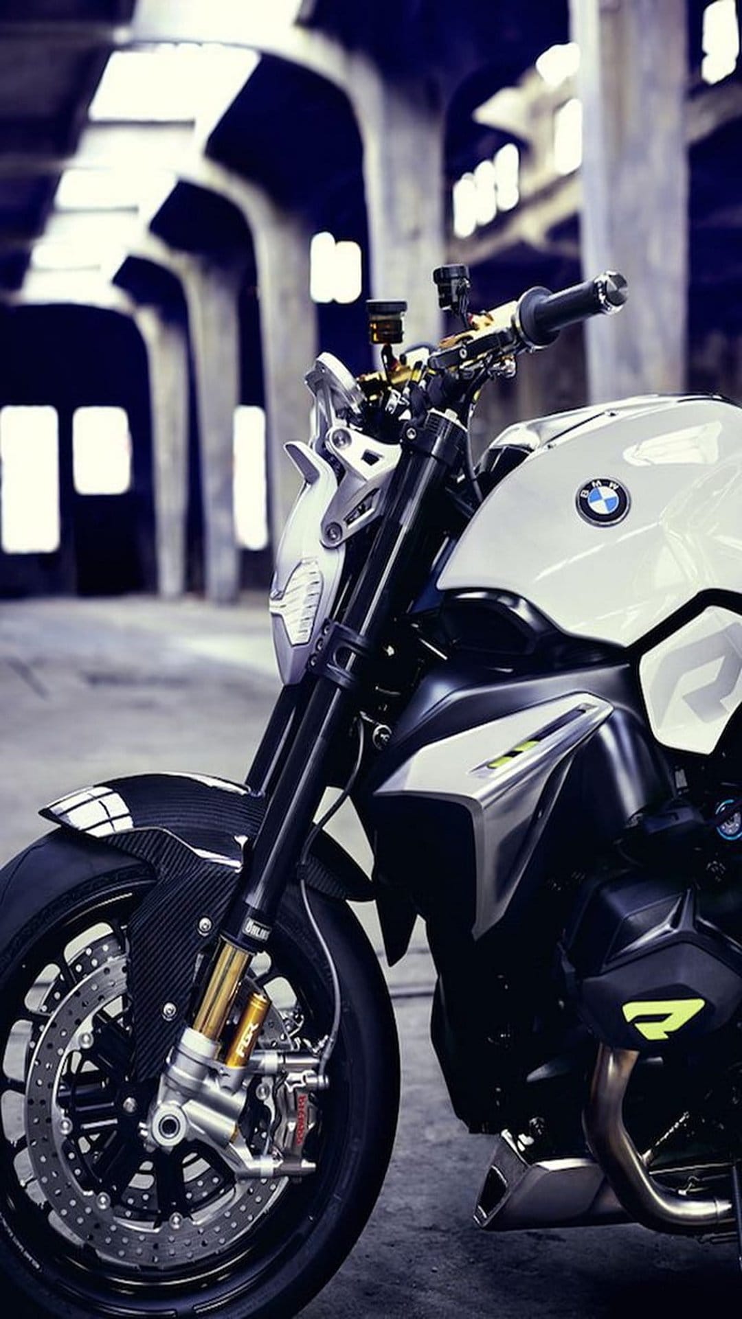 White BMW motorcycle with a carbon fiber fender and LED headlight parked inside a dark, arched industrial building.