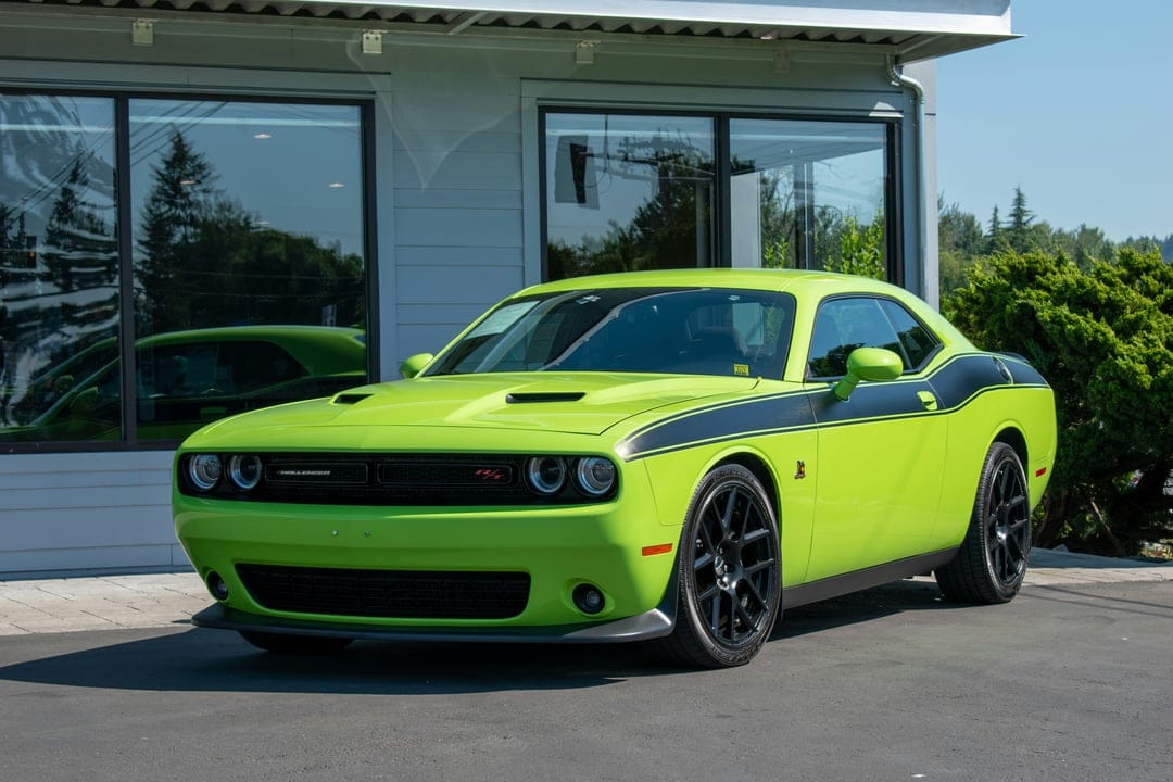Lime green Dodge Challenger R/T Scat Pack with black racing stripes and an aggressive front grille on pavement.