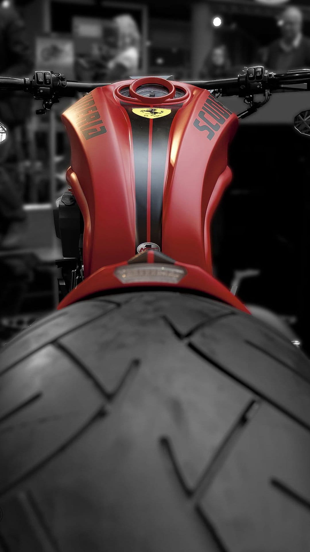 Red Ducati Scrambler motorcycle fuel tank with racing stripes and textured black tires in a low-angle shot.
