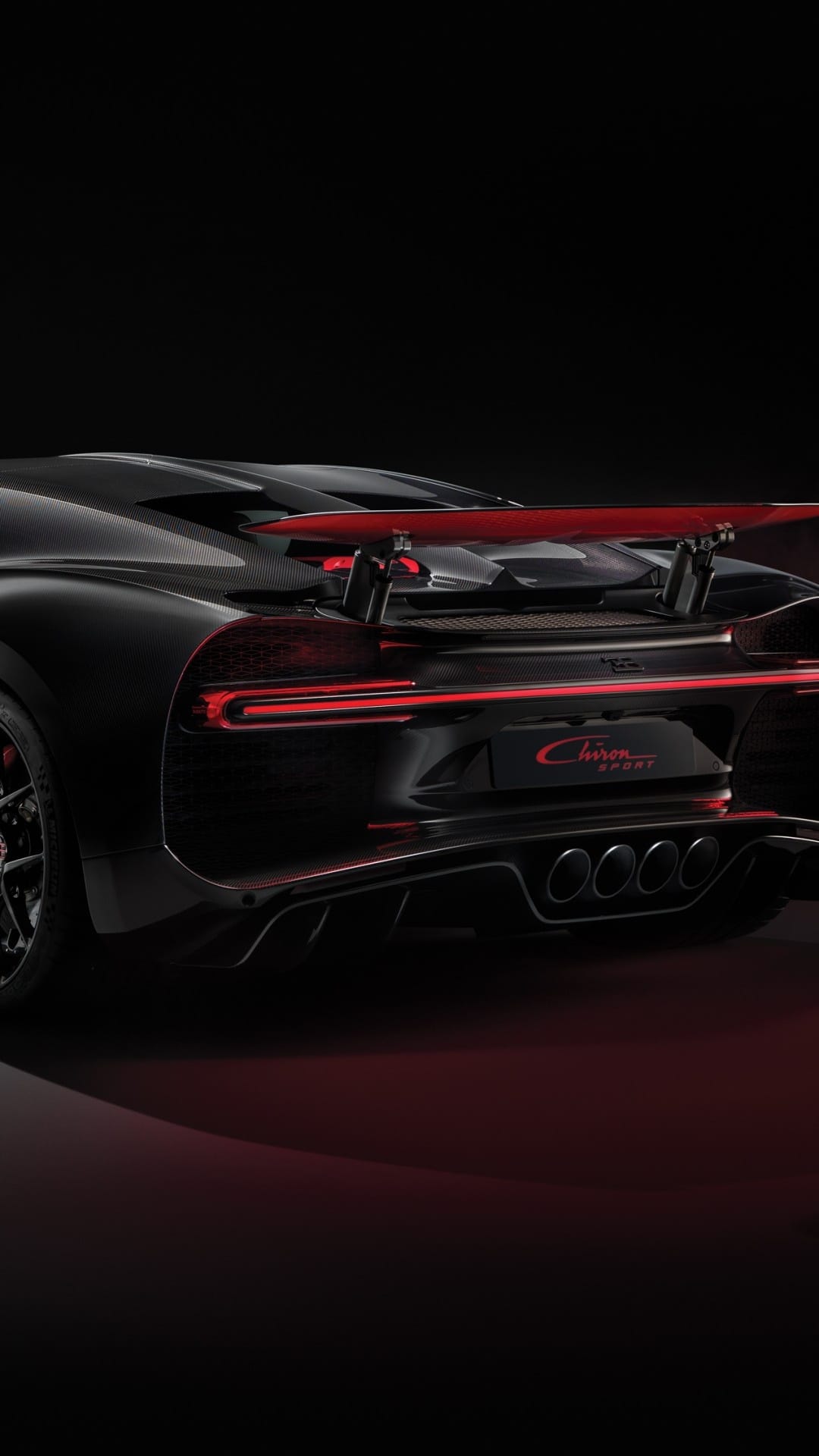 Rear of a black Bugatti Chiron Sport with red LED tail light bar and quad exhausts on a dark background.