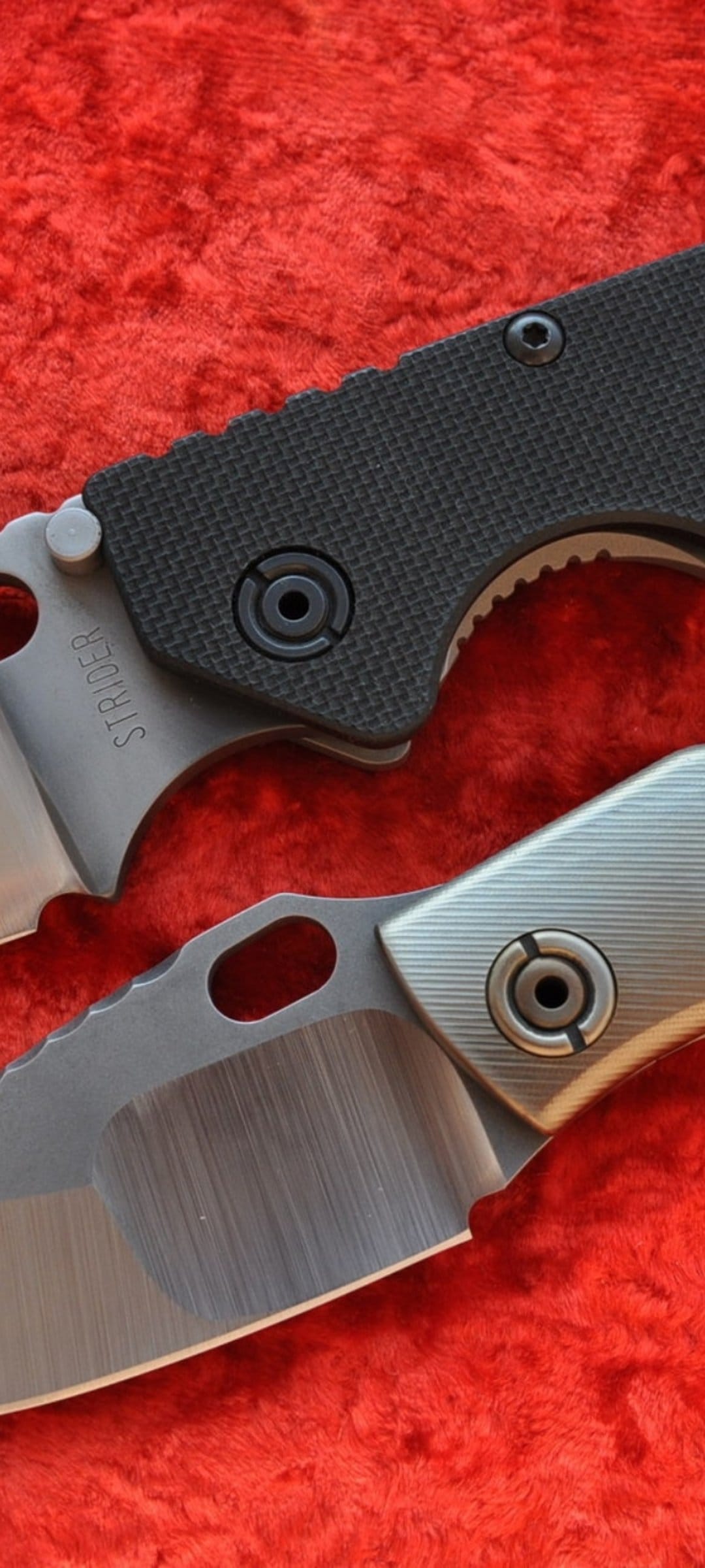 Two tactical folding knives with black and silver handles on a vivid red textured background in a close-up shot.