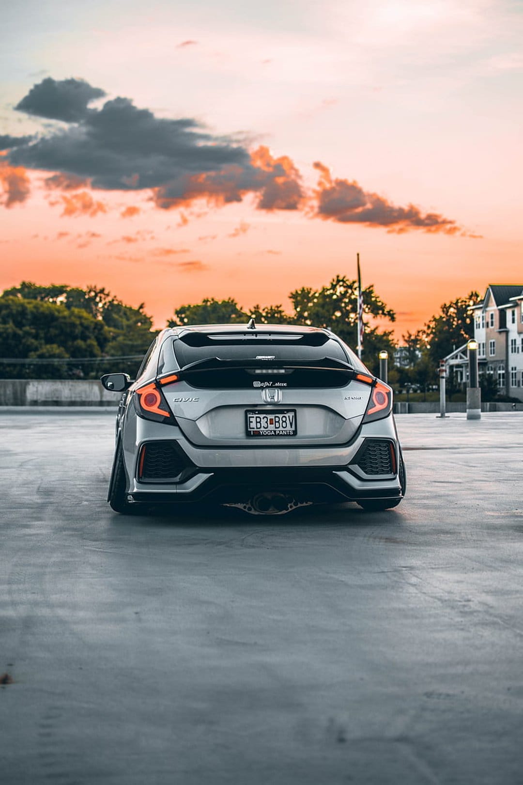 Silver Honda Civic hatchback with modified taillights parked on concrete under an orange and pink sunset sky.