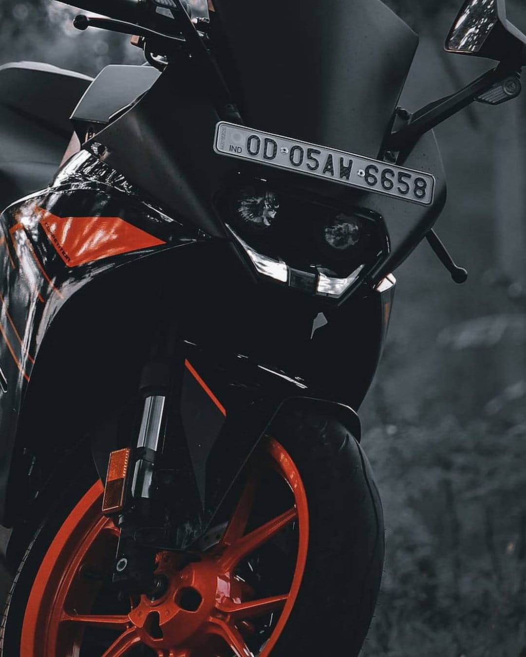 KTM RC motorcycle front fairing with orange graphics and alloy wheels against a blurred grayscale background.