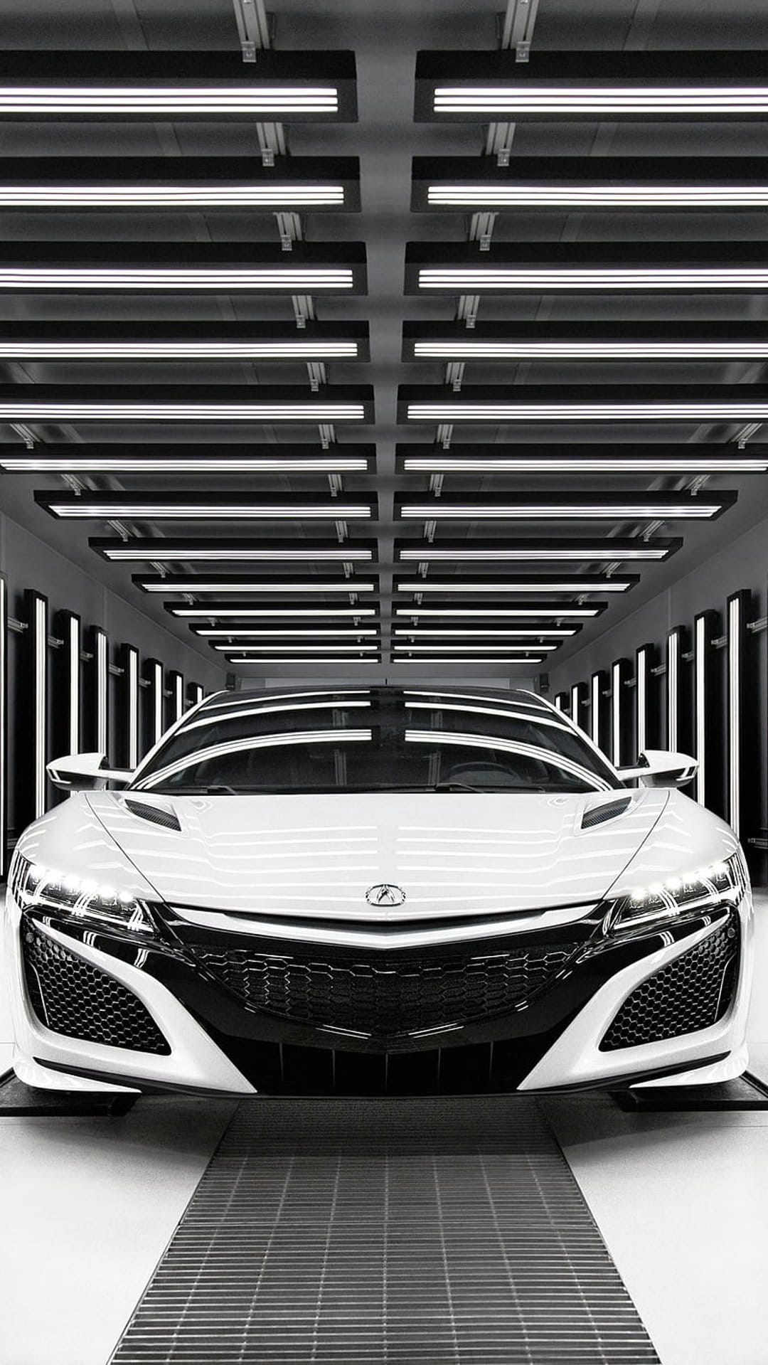 White Acura NSX sports car parked under linear ceiling lights in a dark, contemporary automotive studio.