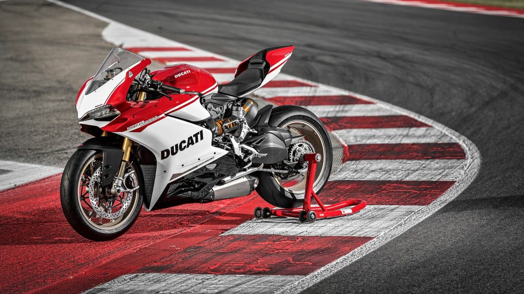 Red and white Ducati 1299 Panigale S Anniversario parked on a racetrack kerb using a rear paddock stand.